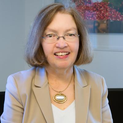 older white woman smiling with shoulder length light hair wearing glasses and a beige blazer with white shirt 