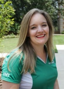 white woman smiling with a green grass backdrop and green shirt