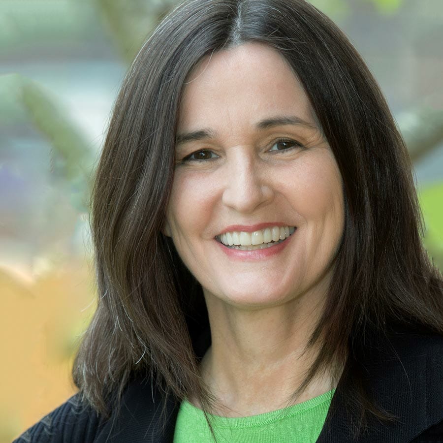 white woman smiling with long brown hair wearing a dark blazer and green shirt