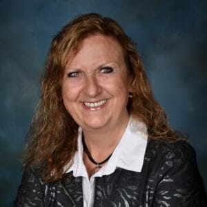 white woman in a white collared shirt and dark grey sweater amid a blue backdrop