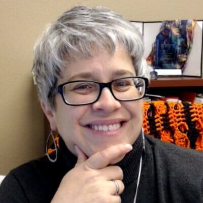 white woman smiling with short grey hair and glasses in a black shirt