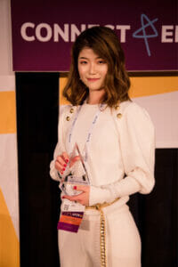 Asian woman holding an award. She has long brown hair and is wearing a white sweater and white pants