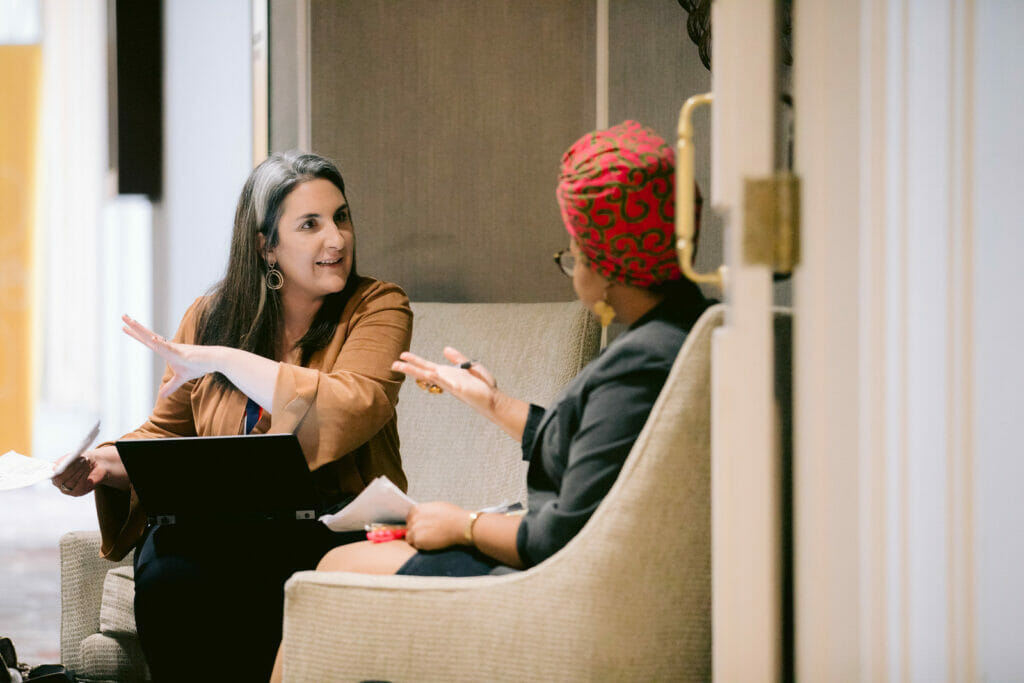 two women sitting and conversing and both have documents in hand