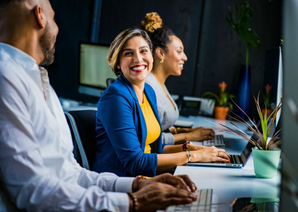 Business people working on laptops and smiling at each other