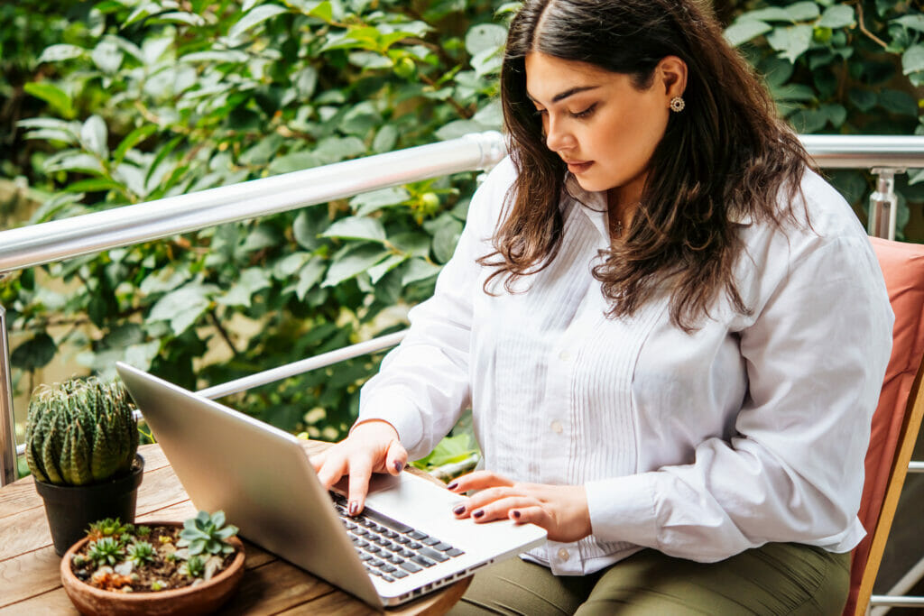 Latina woman in white shirt works on a laptop