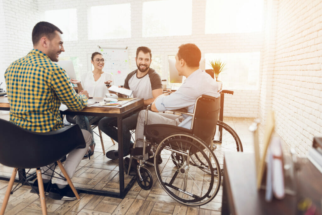 A man in a wheelchair communicates cheerfully with his coworkers during a business meeting.