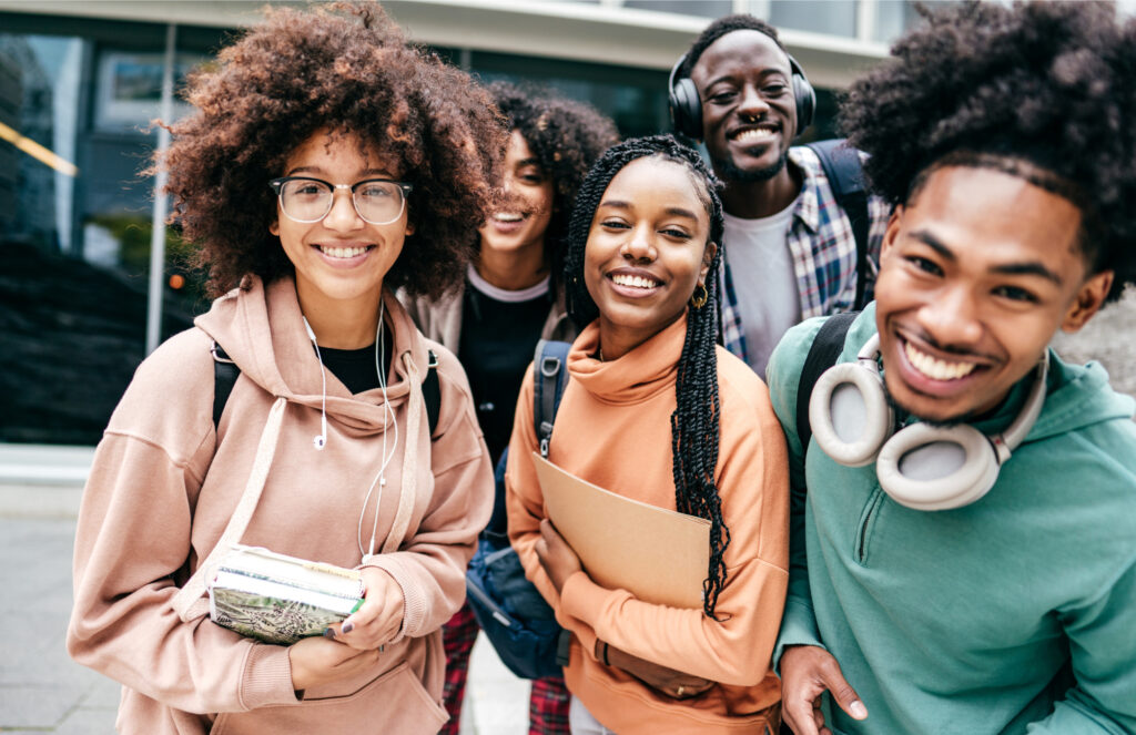 Five black college students smiling in front of a campus building