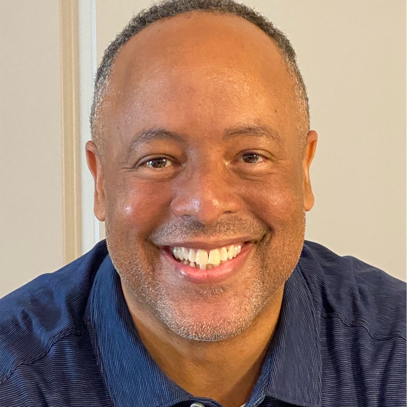 headshot of a smiling black man with short greyish hair wearing a blue polo shirt