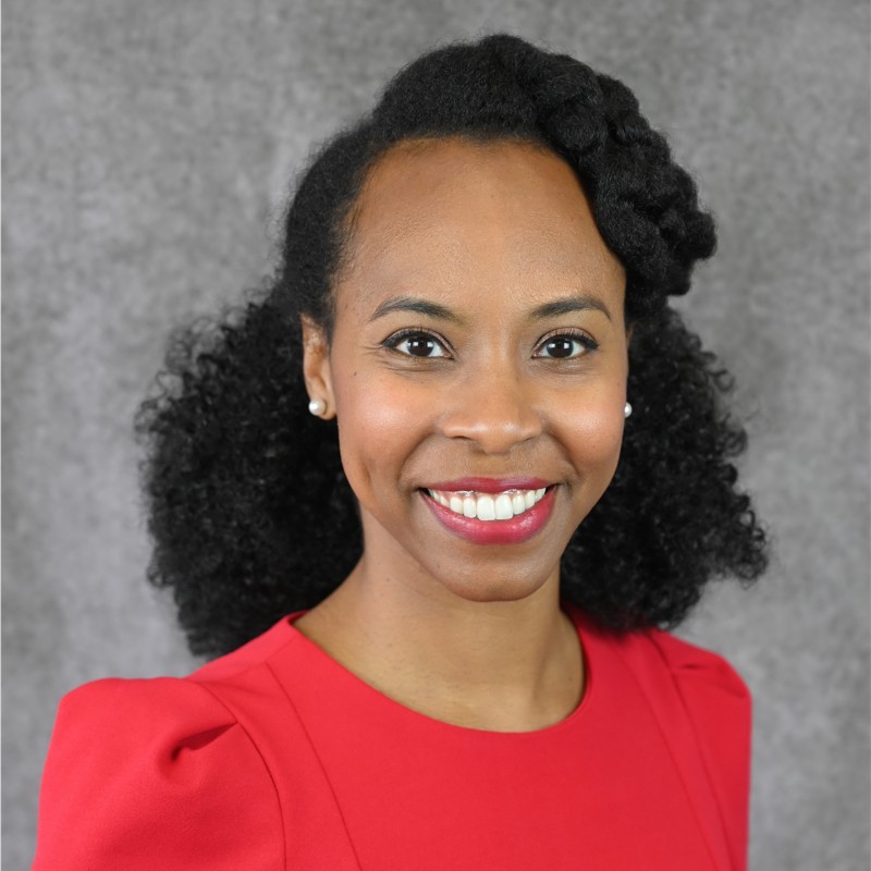 headshot of a smiling black woman with long and curly black hair wearing a red ruffled shirt