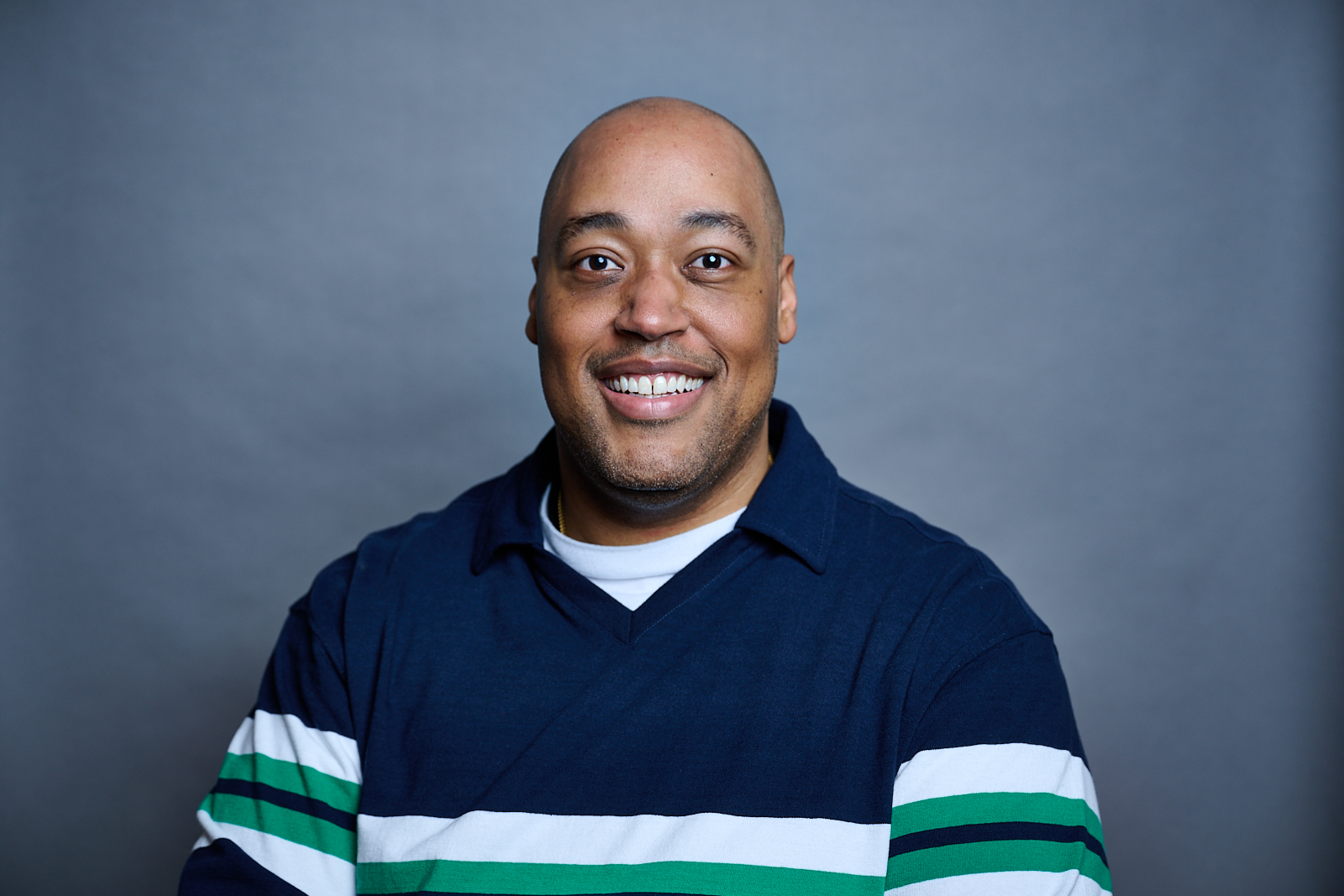 headshot of a smiling black man wearing a color blocked blue, white, and green sweater