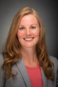 headshot of white woman with long blond hair in a grey blazer and red shirt