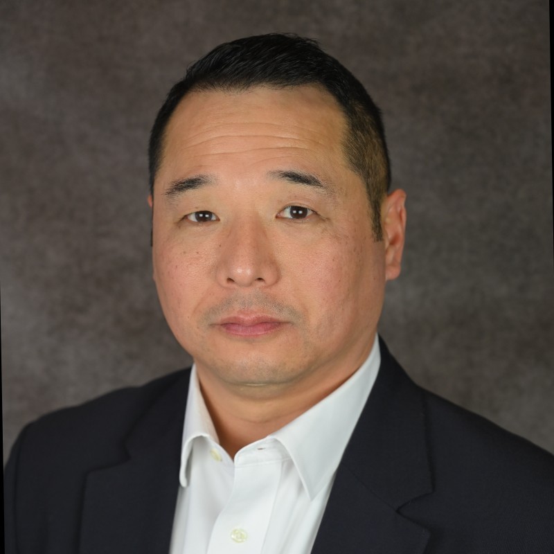 headshot of asian man with short black hair wearing a black blazer and white collared shirt