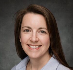 White woman with long brown hair smiling in front of a dark gray background
