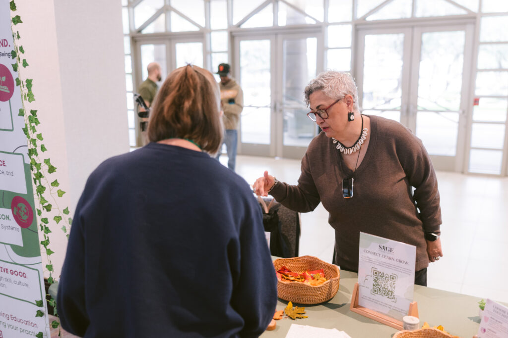 Woman exhibiting discusses her services with another woman at Symposium