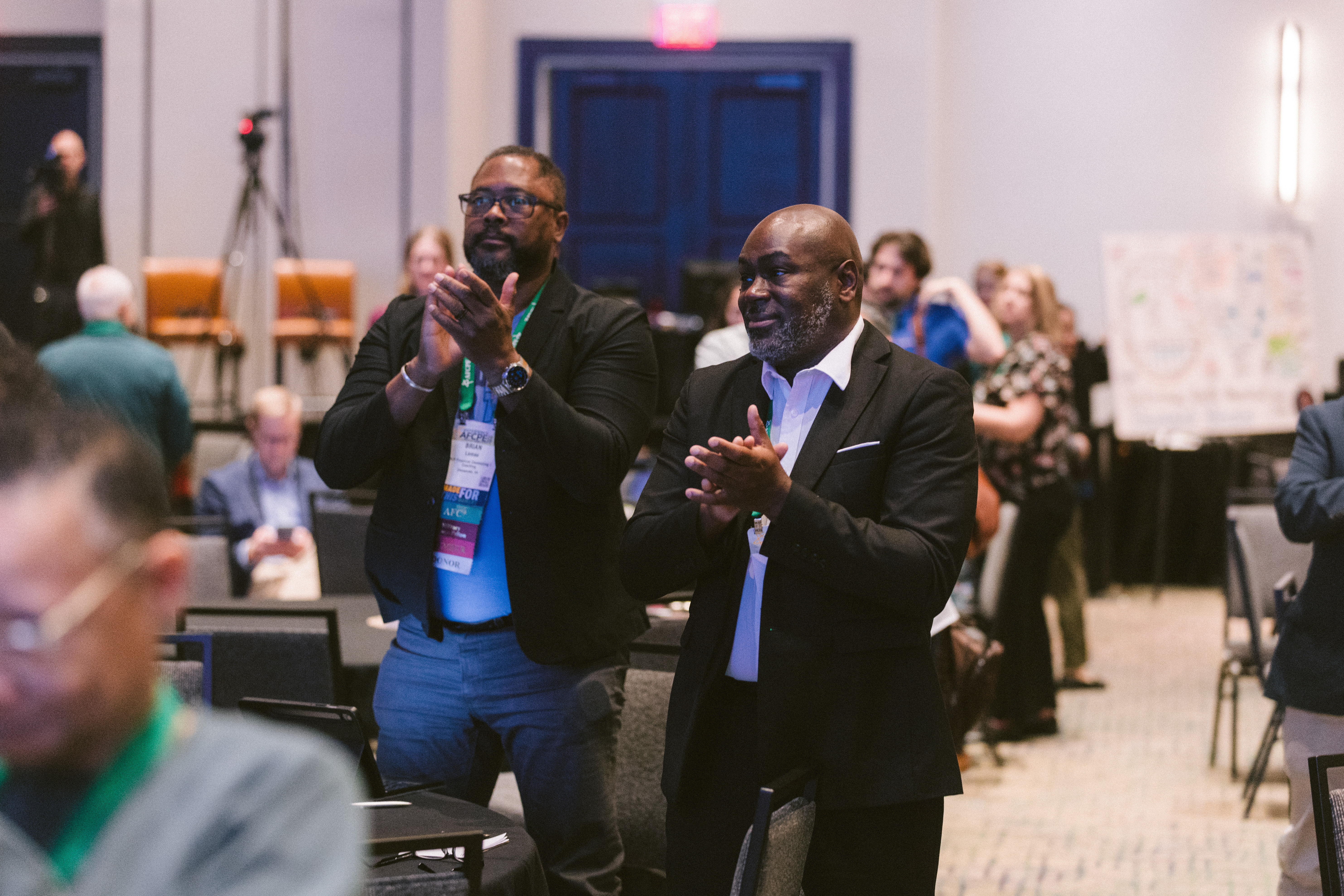 Two men of color standing and applauding at Symposium