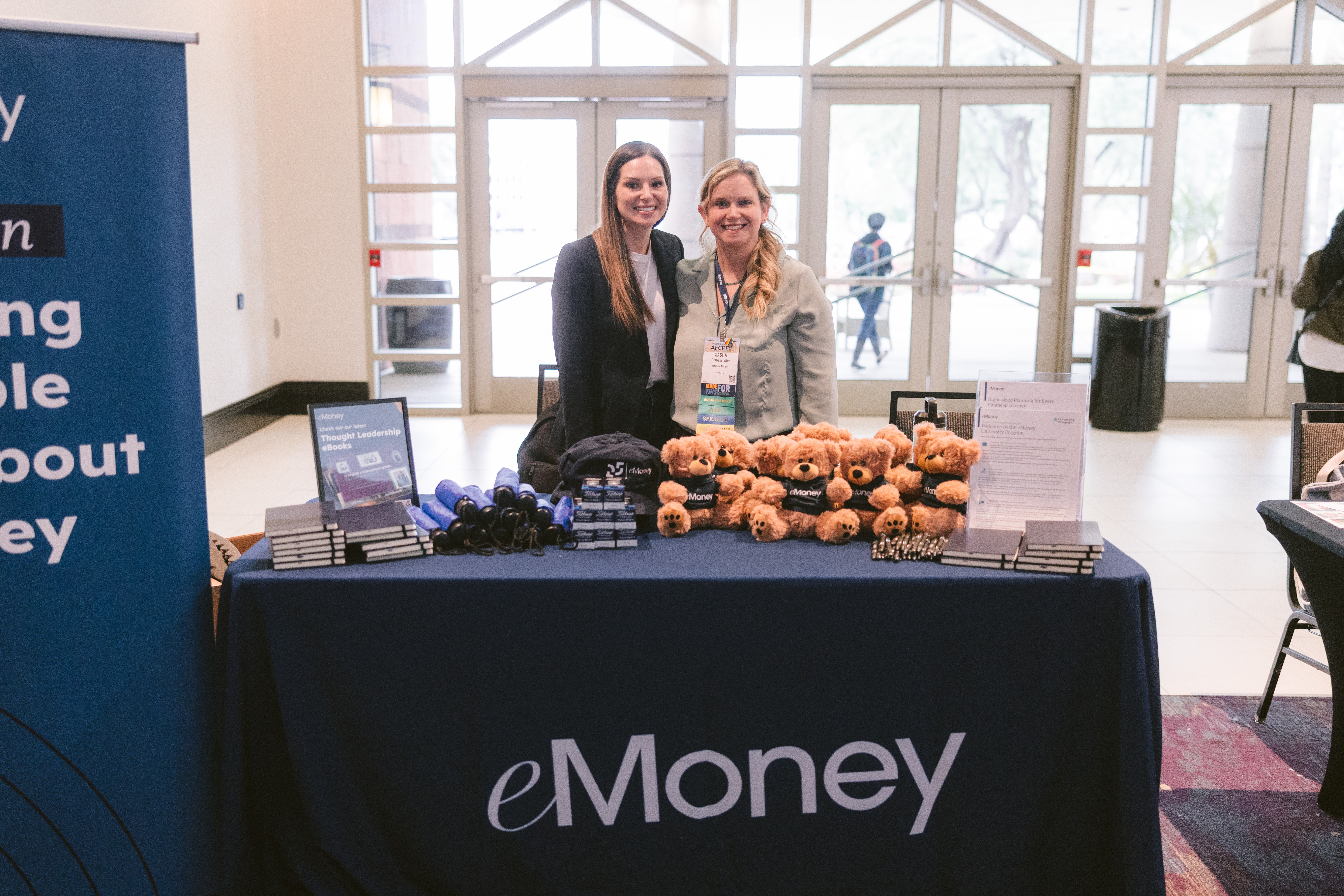 Two women smiling while exhibiting at Symposium