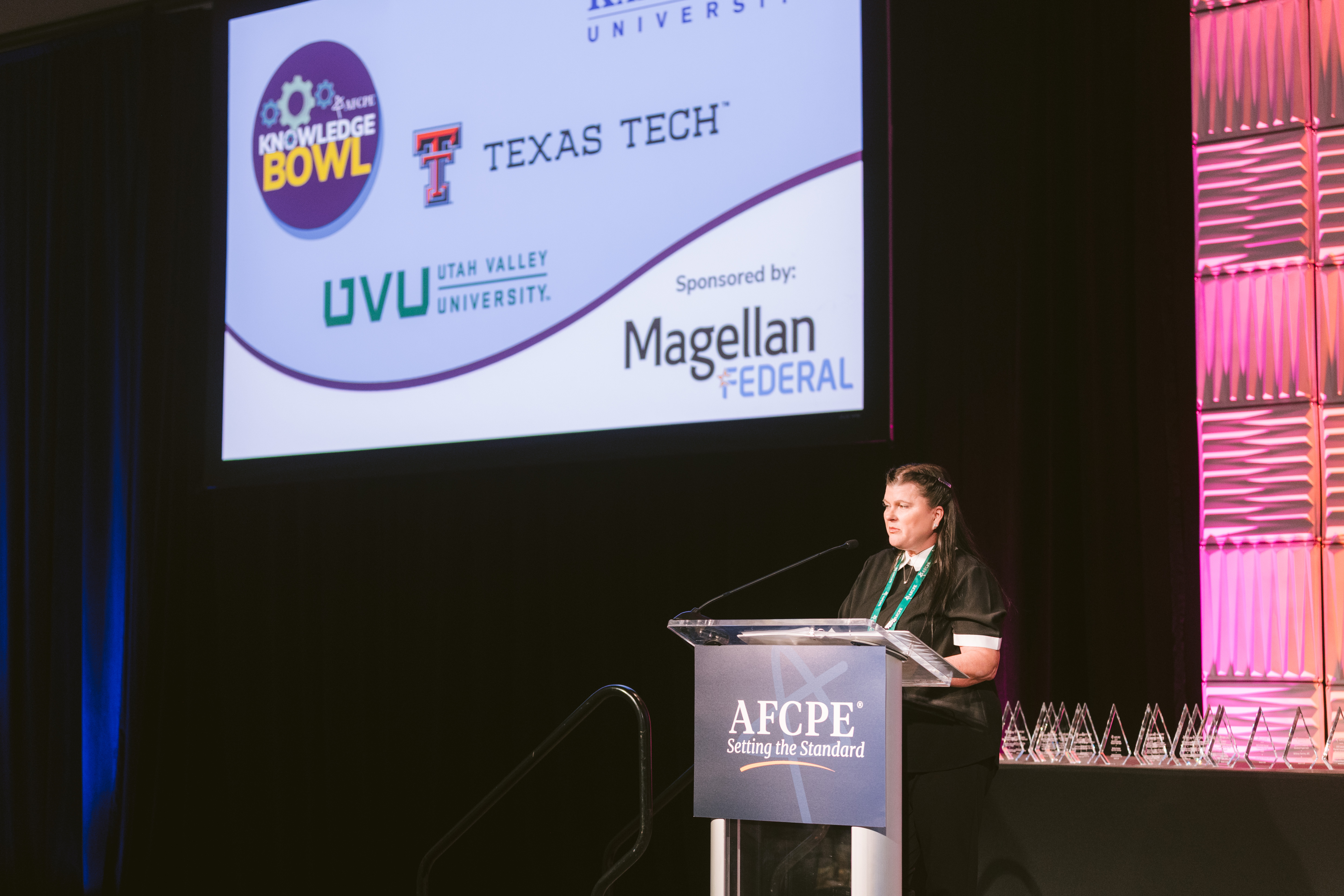 Person on stage announcing the Knowledge Bowl winners sponsored by Magellan Financial at Symposium