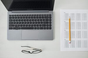 An open laptop, glasses, pencil and a test answer sheet on a white desk