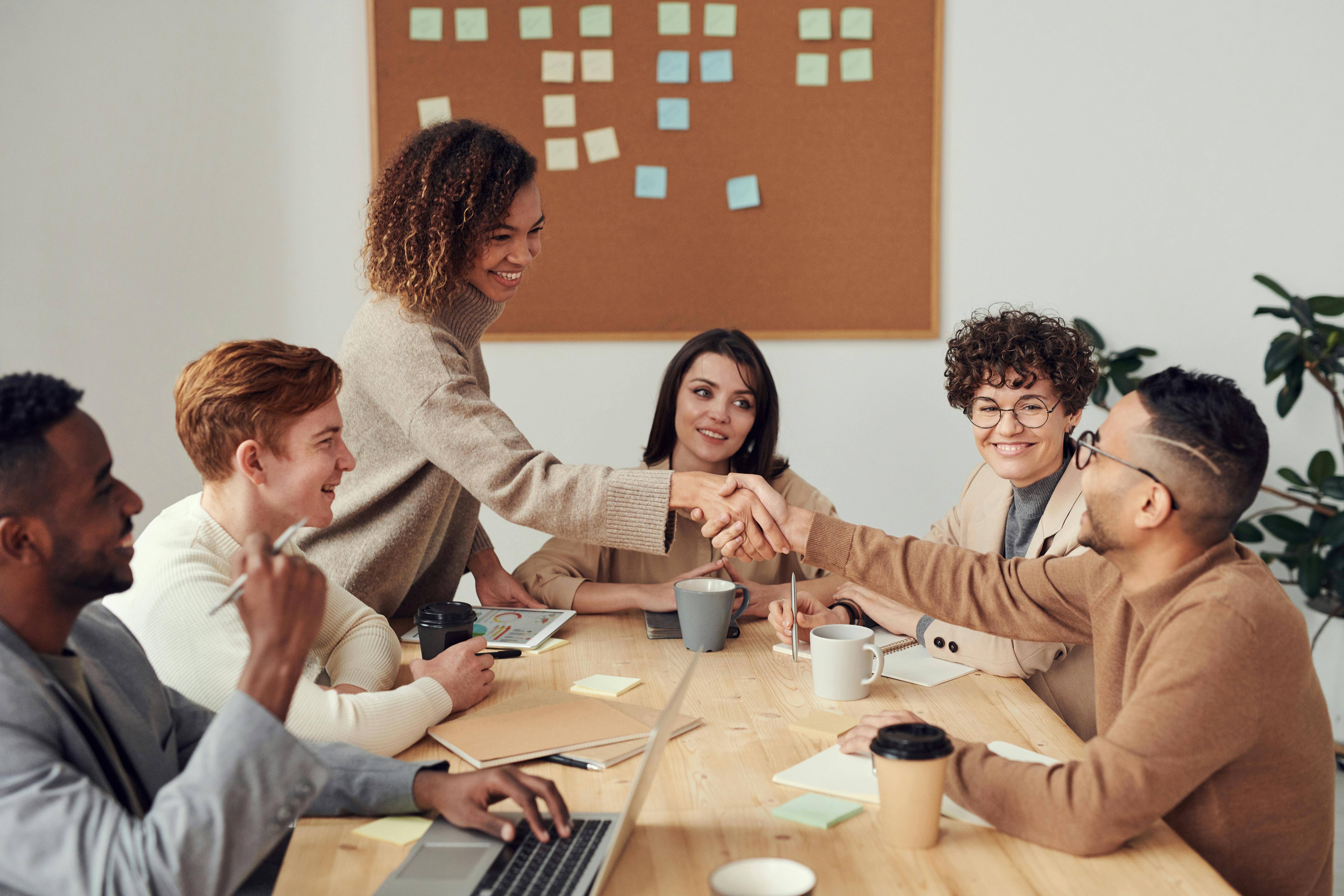 woman shaking a man's hand in a group office meeting