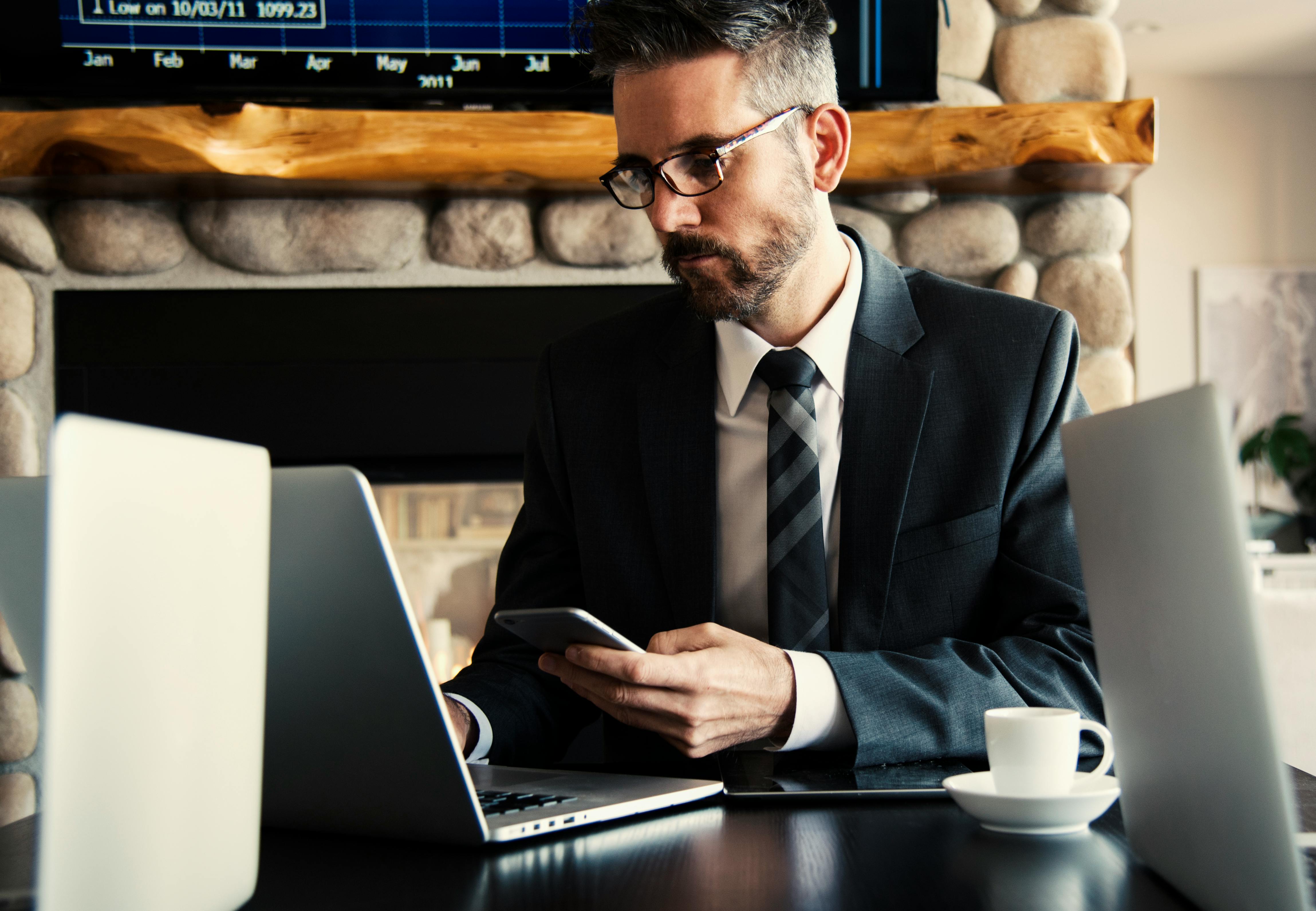man in a suit on his phone and working in a coffee shop on his laptop