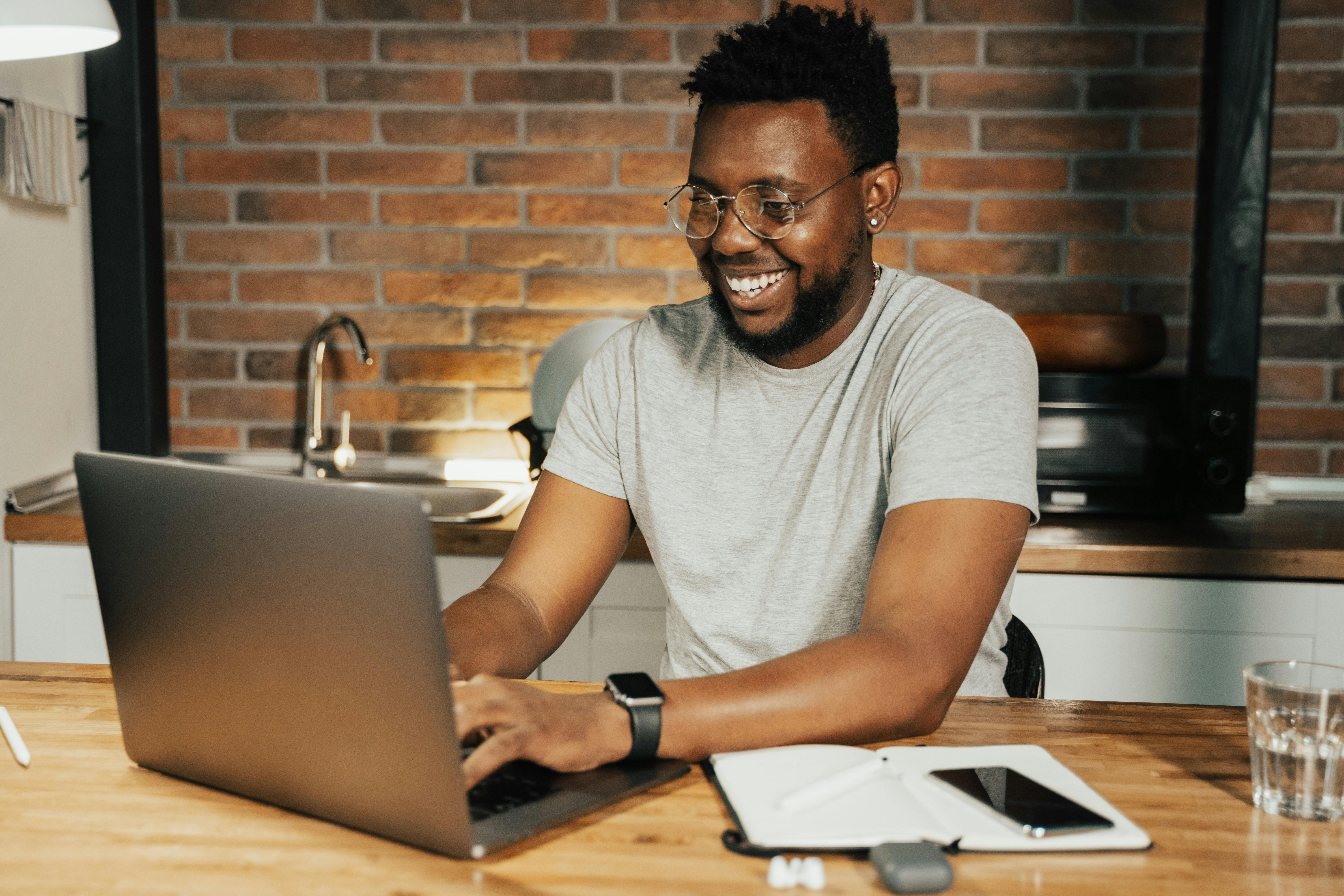 Man of color on his laptop smiling as he chats with someone online.