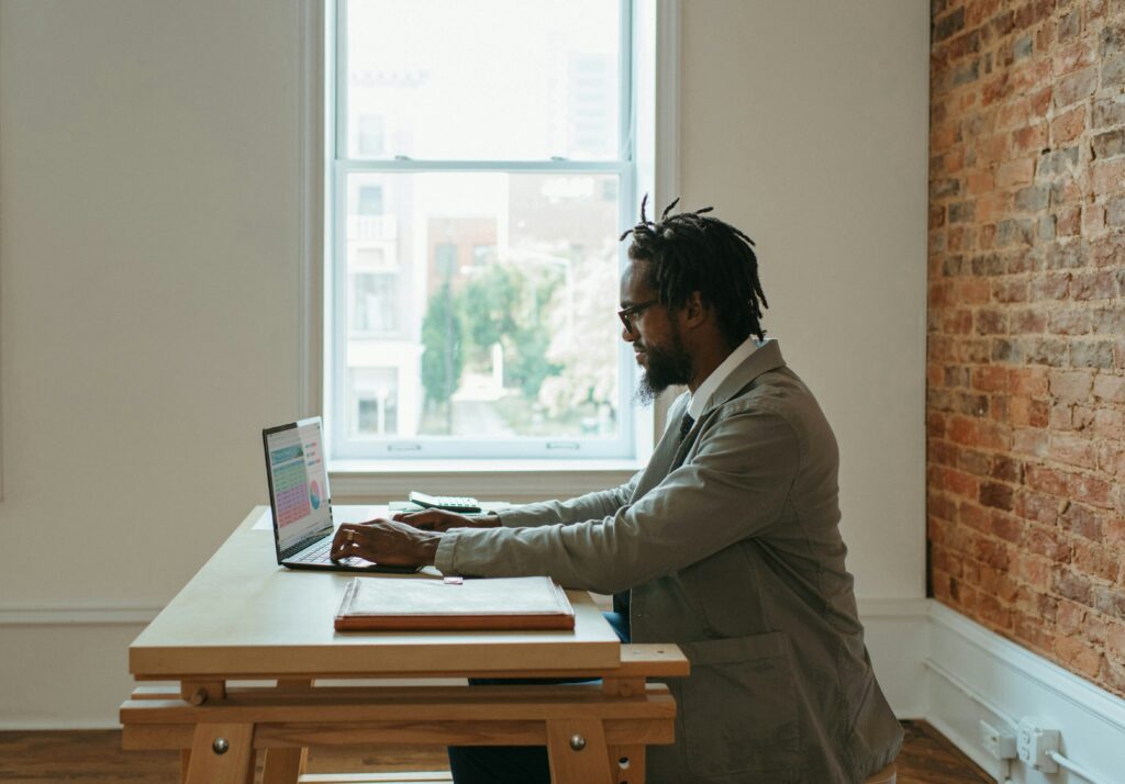 man of color at his computer in his office, brick wall behind him