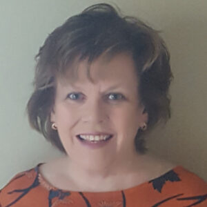 white woman smiling with short light brown hair wearing a red and black shirt with a beige background