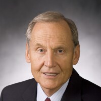 older white man with light hair wearing a dark suit, white collared shirt and dark tie
