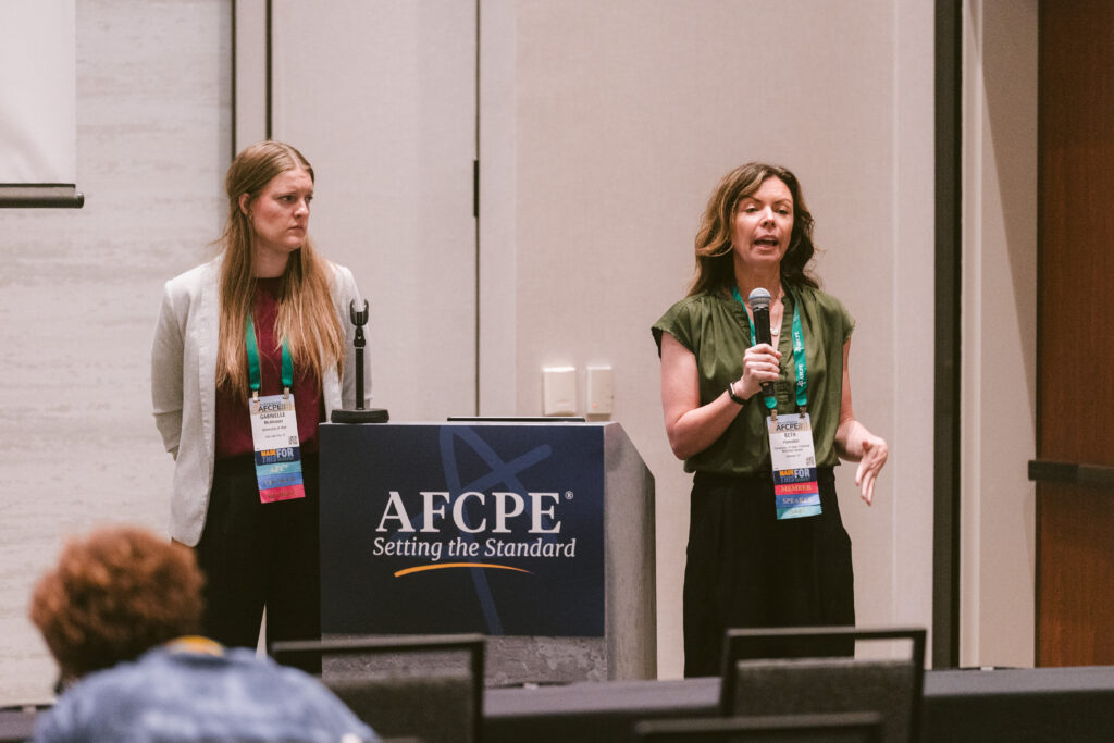 Two women standing in front of attendees presenting research at Symposium