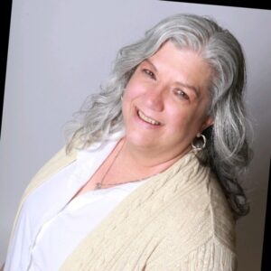 headshot of white woman with grey long hair and white shirt and beige cardigan