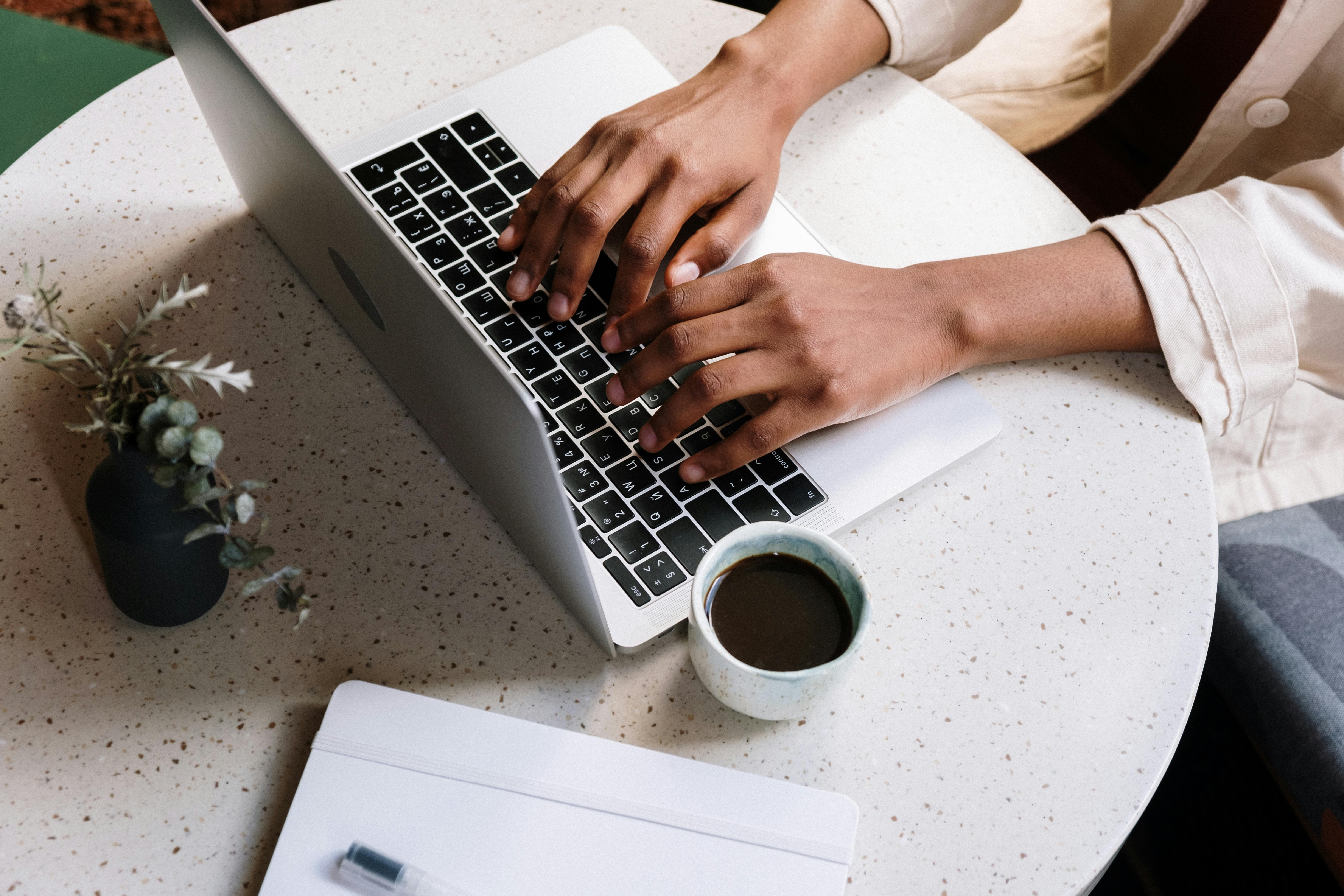 hands of a woman of color blogging on her laptop with coffee