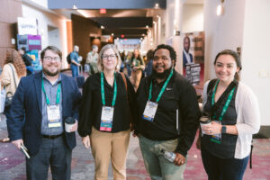 diverse group of four people smiling in the busy hallway of Symposium