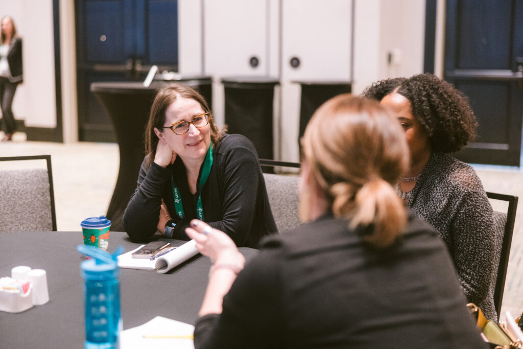 two white woman, one with only the back of her head visible, and a black woman in a meeting at an event