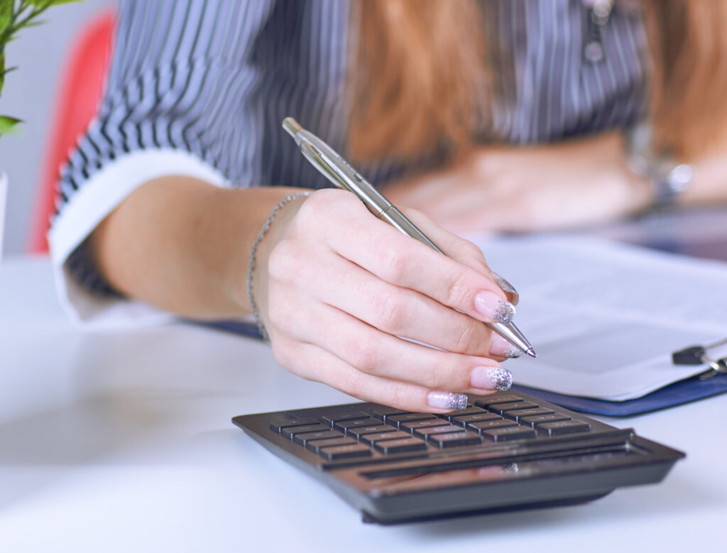 Business woman hand using a calculator with silver pen in office closeup. Business finance and education concept.