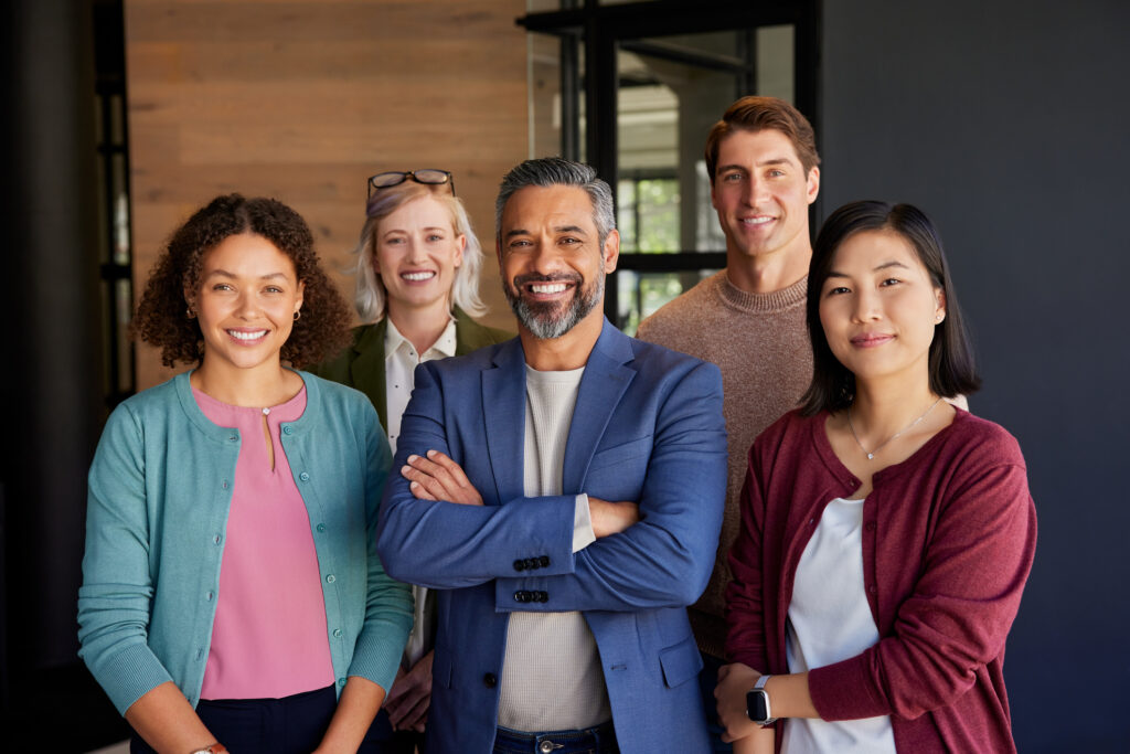 Group of diverse professionals posing in an office environment while smiling and looking at camera. Successful business group posing together at modern office. Middle eastern leadership with his multiethnic team expressing unity and confidence.