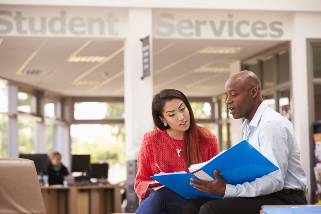 College Student Having Meeting With Financial Aid professional To Discuss Work Looking At File