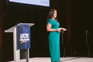 Woman in green pant suit on stage at Symposium.