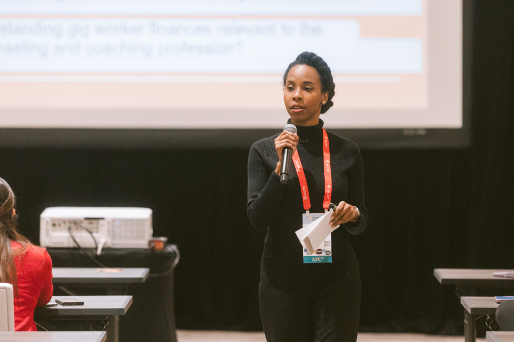 black woman wearing all black holds a microphone while giving a presentation