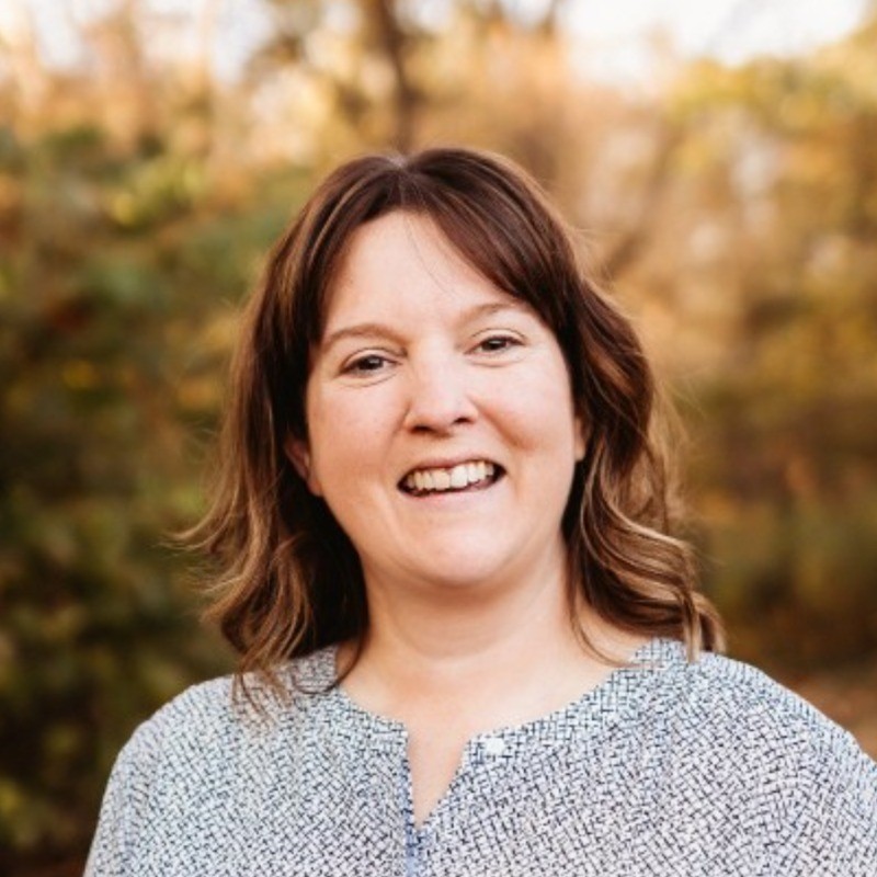 Woman smiling in front of a background of faded trees.