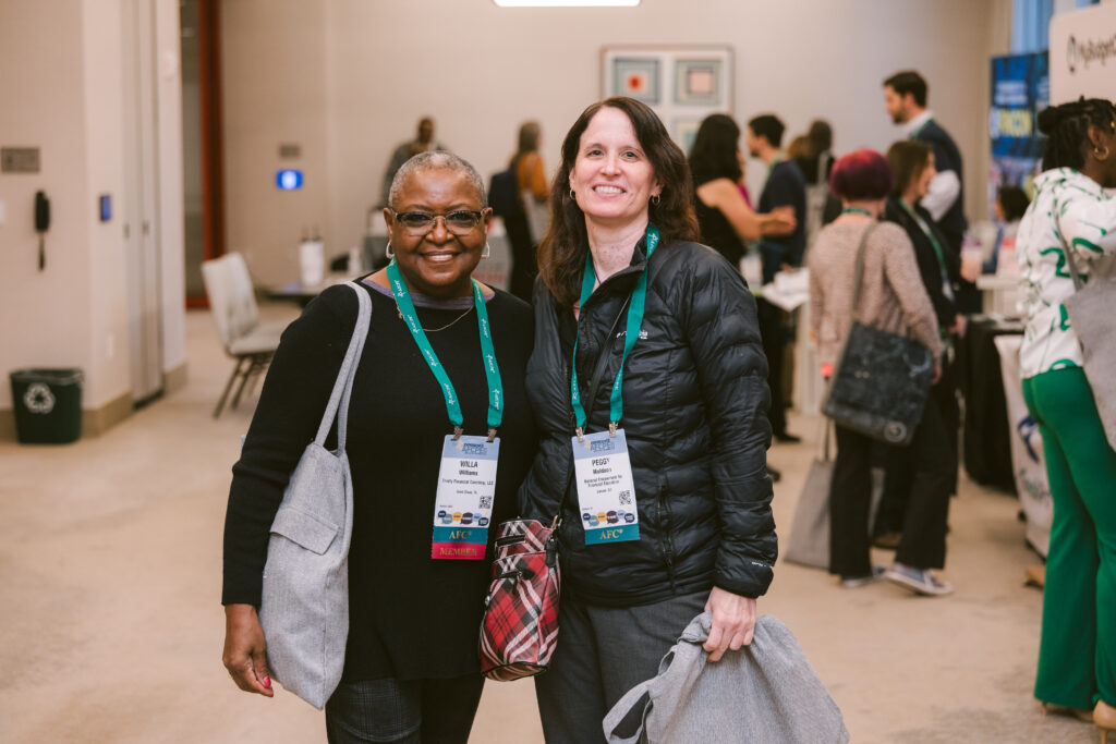 A black woman and a white woman smiling during a break at Symposium.