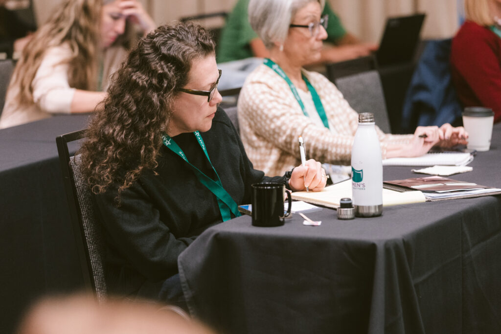 White woman with long wavy brown hair taking notes at a conference