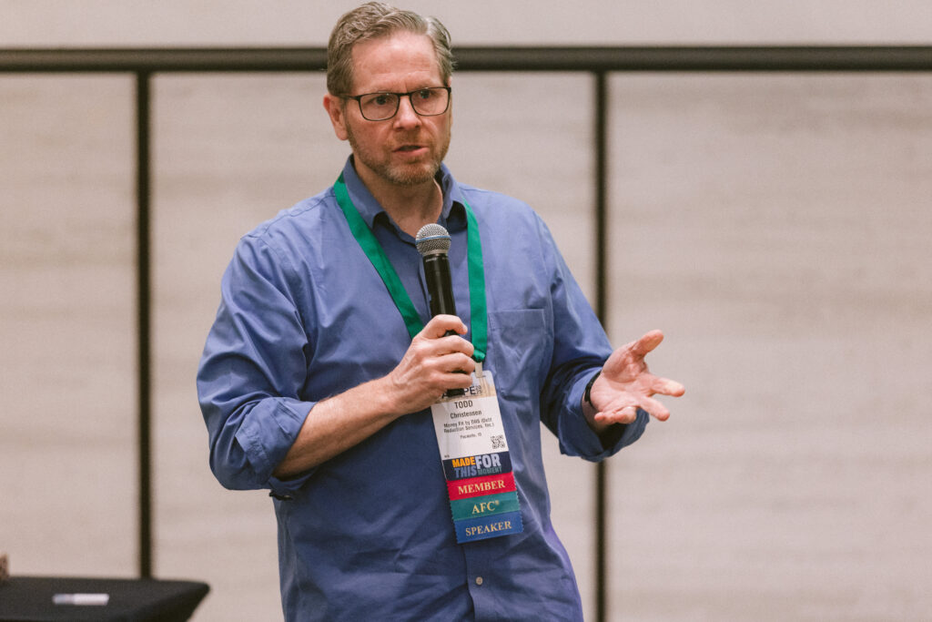 white man in a blue button down shirt holding a microphone while giving a presentation