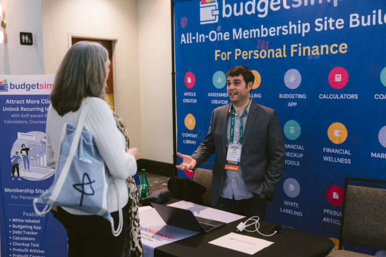 Photo of man talking to woman in front of Budget Coach exhibiting table at Symposium.