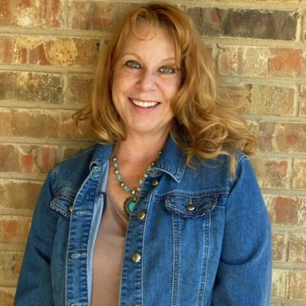 white woman with long reddish hair in a denim jacket smiling