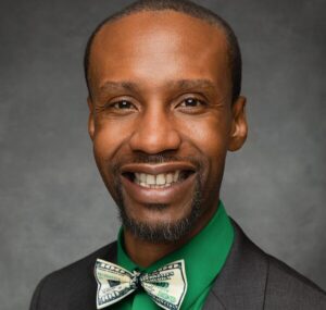 Dark background, man of color, light colored bow tie, green shirt, dark blazer