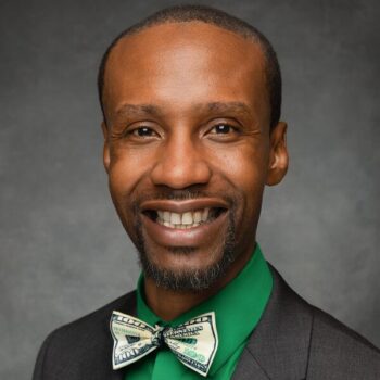 Dark background, man of color, light colored bow tie, green shirt, dark blazer