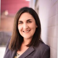 headshot of white woman with long brown hair in a dark grey blazer