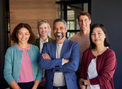 Group of diverse professionals posing in an office environment while smiling and looking at camera. Successful business group posing together at modern office. Middle eastern leadership with his multiethnic team expressing unity and confidence.