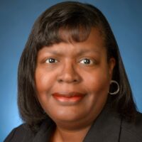 Headshot of black woman with shoulder length dark hair wearing a dark shirt with a blue backdrop
