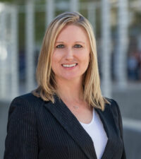 white woman in a dark blazer over a white t-shirt with an office building backdrop